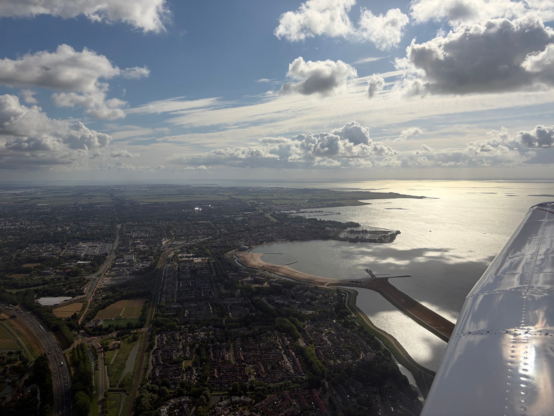 De kustlijn en het glinsterende IJsselmeer over de vleugel van de Piper